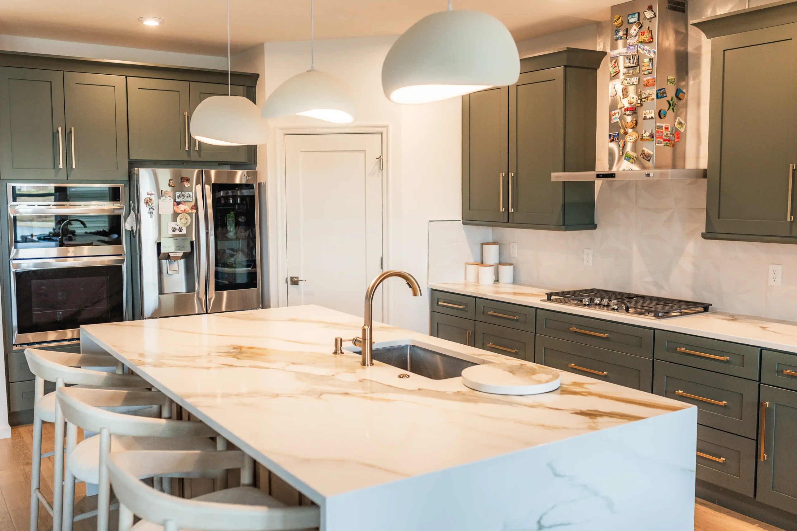 Waterfall quartz island with warm gold veining, seating and pendant lighting, set against deep green shaker cabinets
